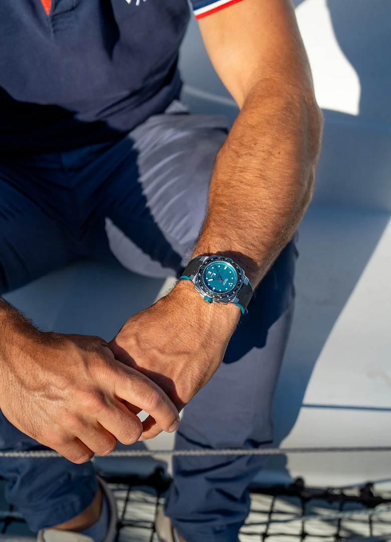 Poignet d'Eric Péron portant l'Alpina Seastrong Diver Extreme Route du Rhum à cadran turquoise, à bord de son trimaran
