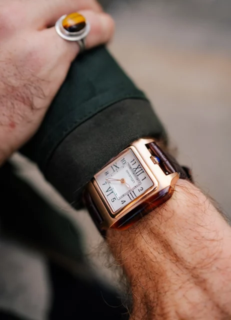 La montre Briston en acétate au poignet, sous une manche de veste cirée verte