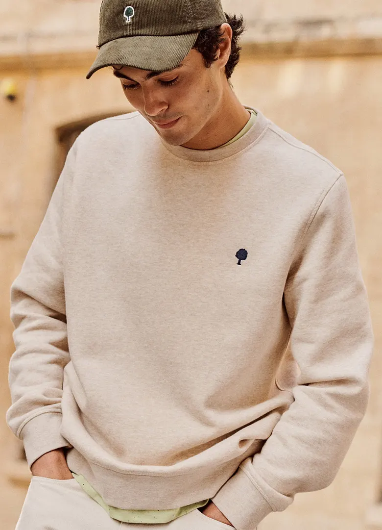 Sweat homme Faguo Donzy beige chiné à col rond avec broderie arbre, porté avec une casquette en velours