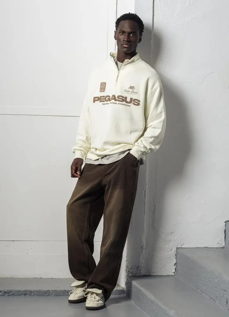 Sweat demi-zip homme Goodies Sportive New Pegasus écru à inscription marron, porté avec un pantalon large
